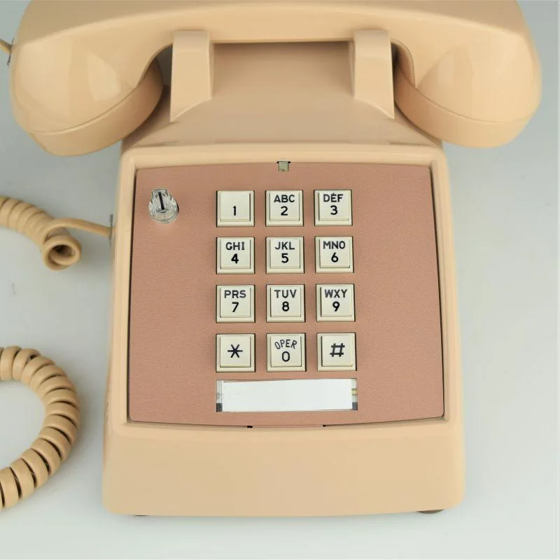 Beige rotary-style push-button telephone with a coiled cord, keypad with numbers and letters, and a metallic switch on the top left of the keypad.