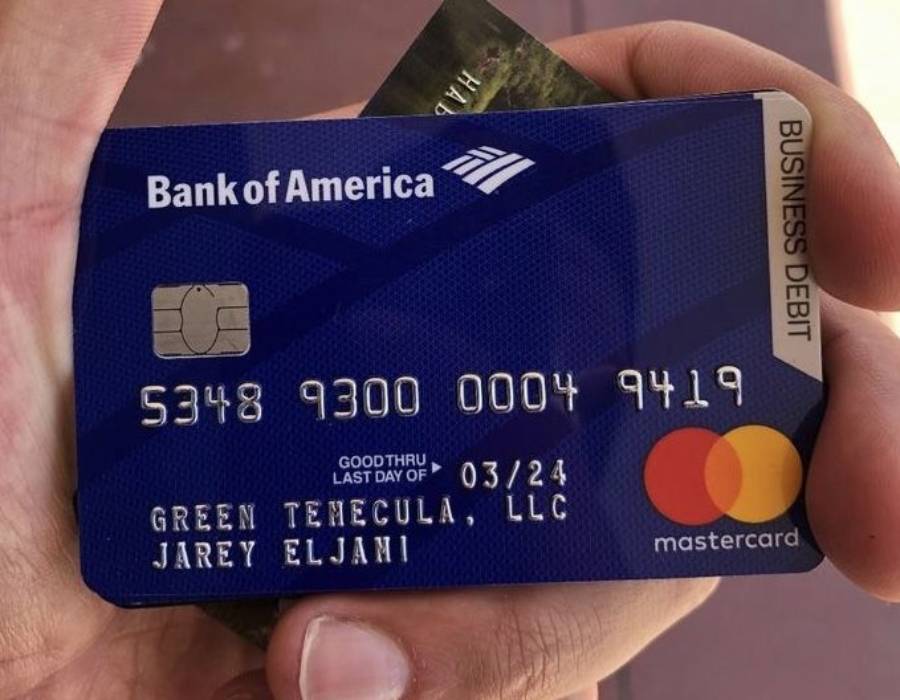 A hand holding a blue Bank of America business debit Mastercard with the name “Green Temecula, LLC Jarey Eljani” and card numbers visible.