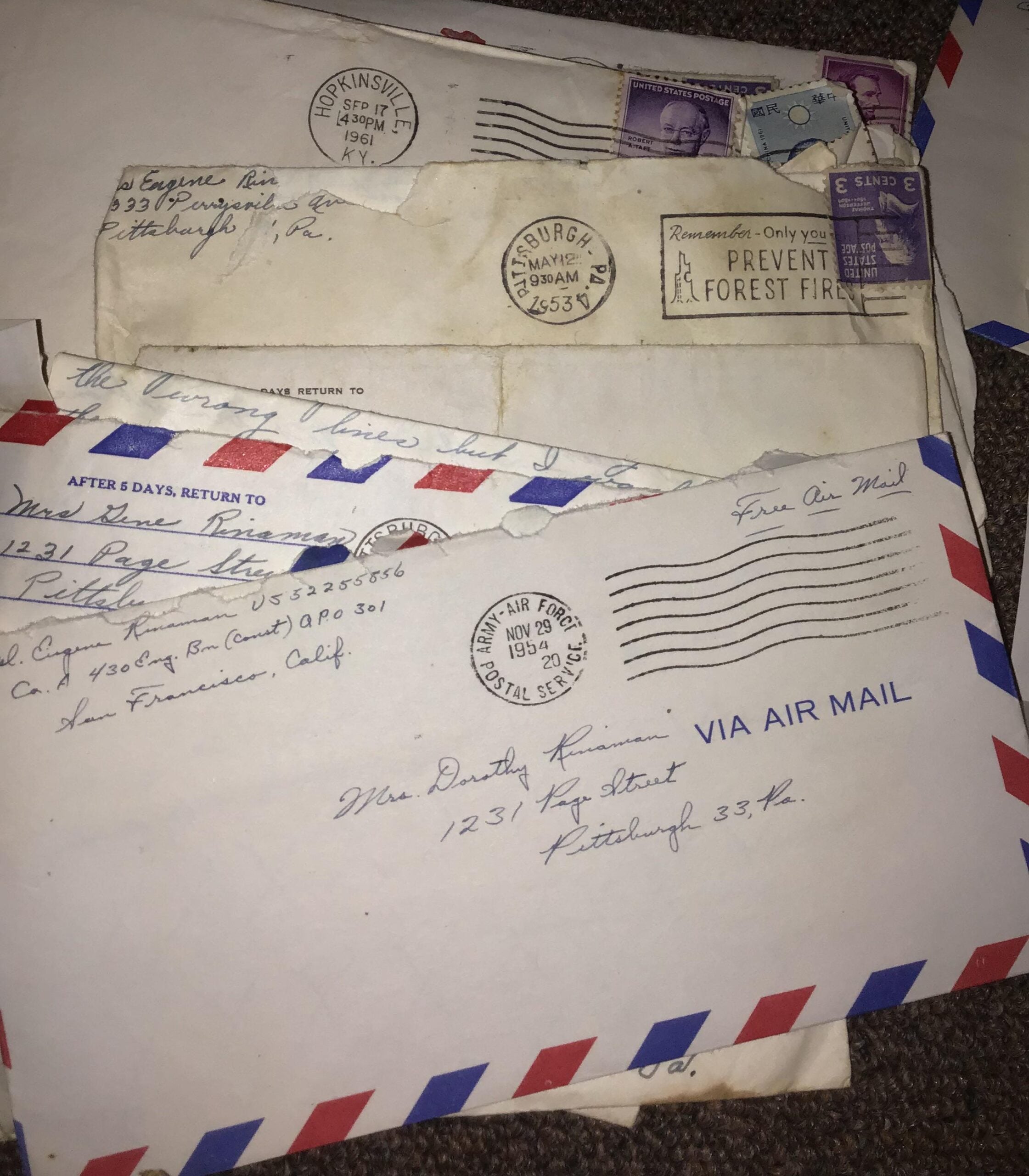 A stack of vintage airmail envelopes with handwritten addresses and postage stamps, some showing postmarks from the 1950s. The envelopes are slightly worn and laid out on a brown textured surface.