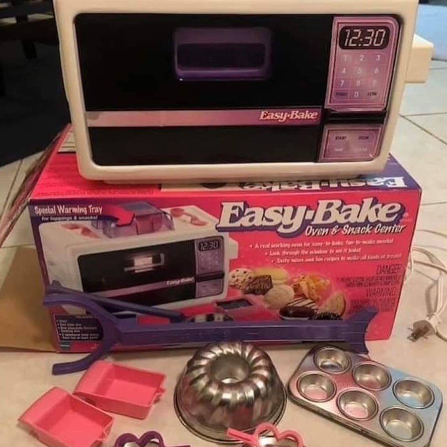 Easy-Bake Oven and Snack Center with accessories, including baking trays, pans, and utensils, displayed next to the product’s colorful box showing baked treats and branding.