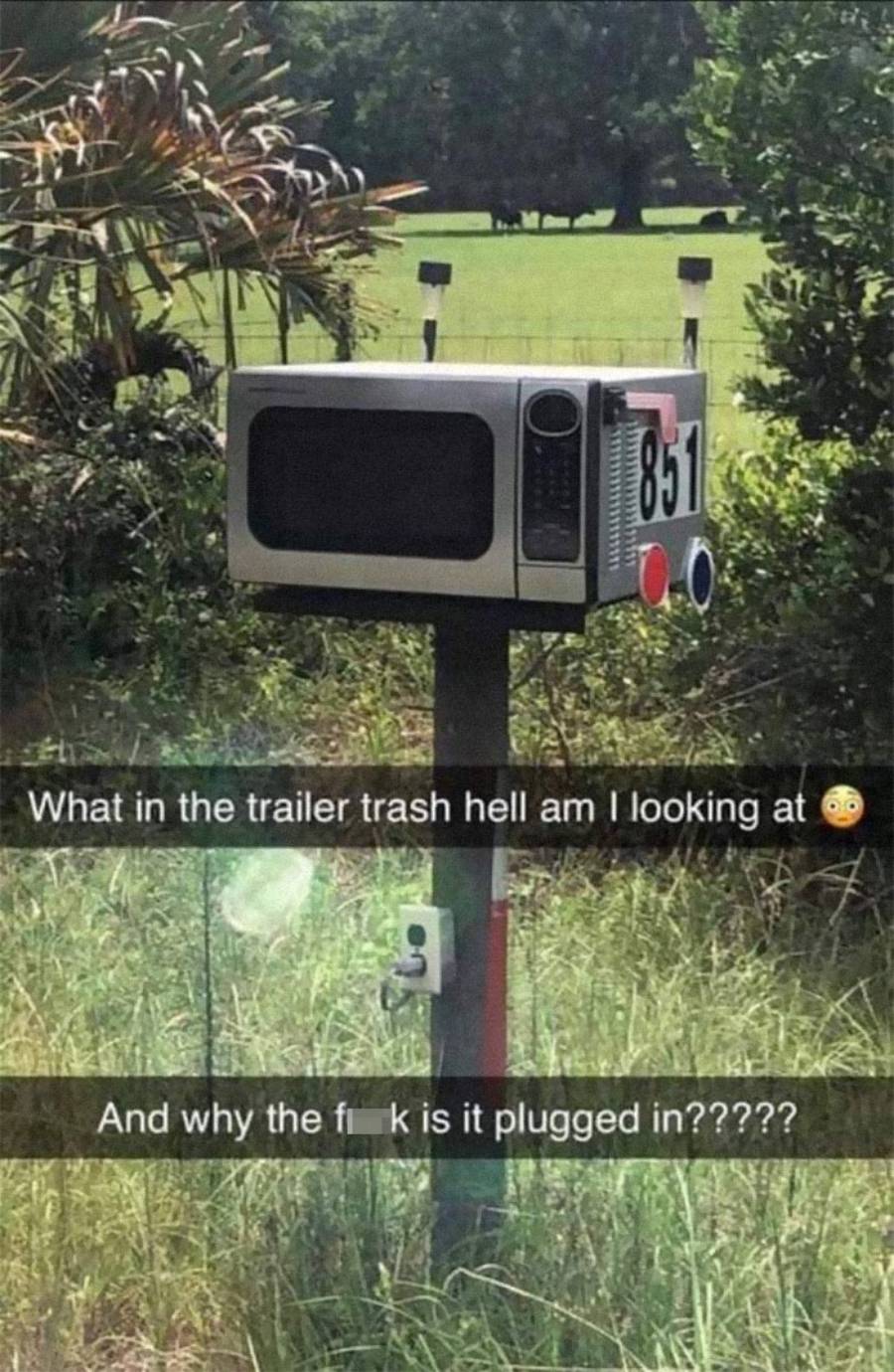 A black microwave is mounted on a post like a mailbox with house number 851. There's a plug socket attached below it, surrounded by grass and trees. Text captions express surprise and confusion.