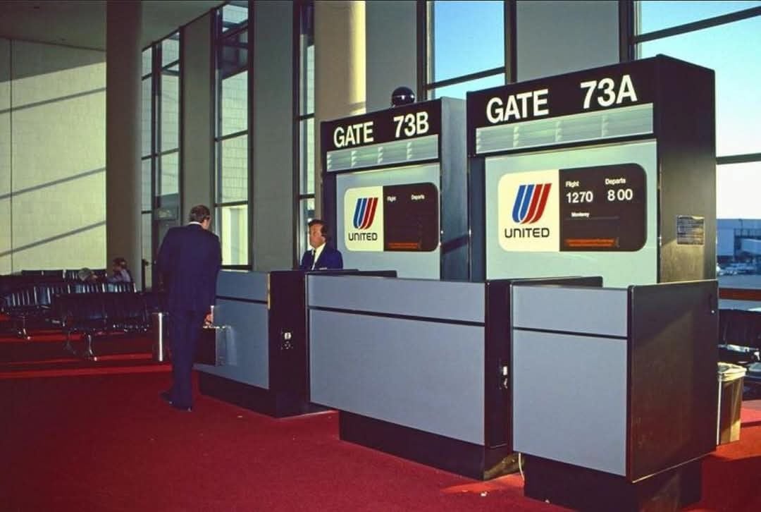 A man speaks with an airline agent at United boarding gates 73A and 73B in an airport terminal with red carpet and large windows.