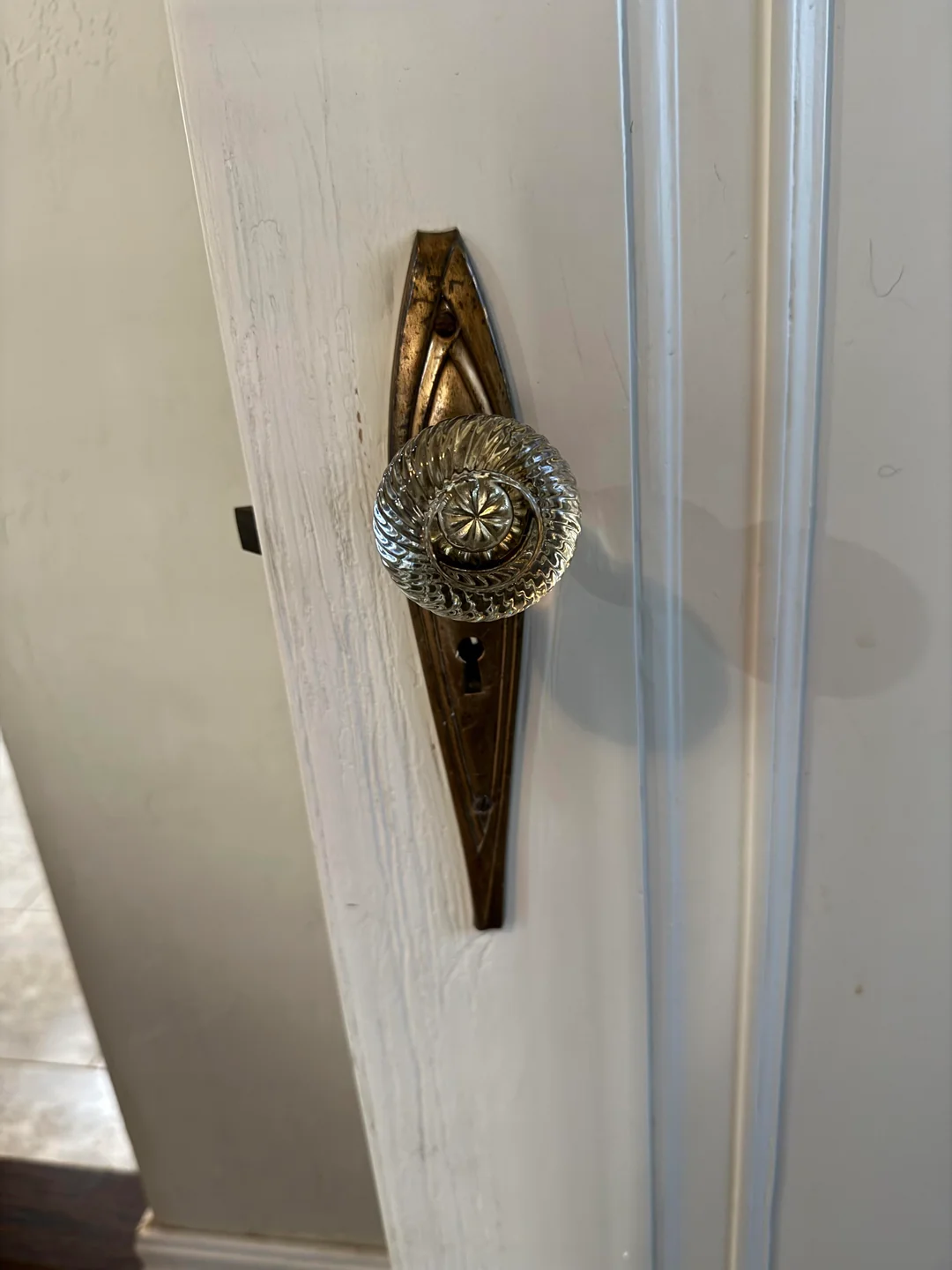 A vintage brass door plate with an ornate glass doorknob and keyhole on a white wooden door.