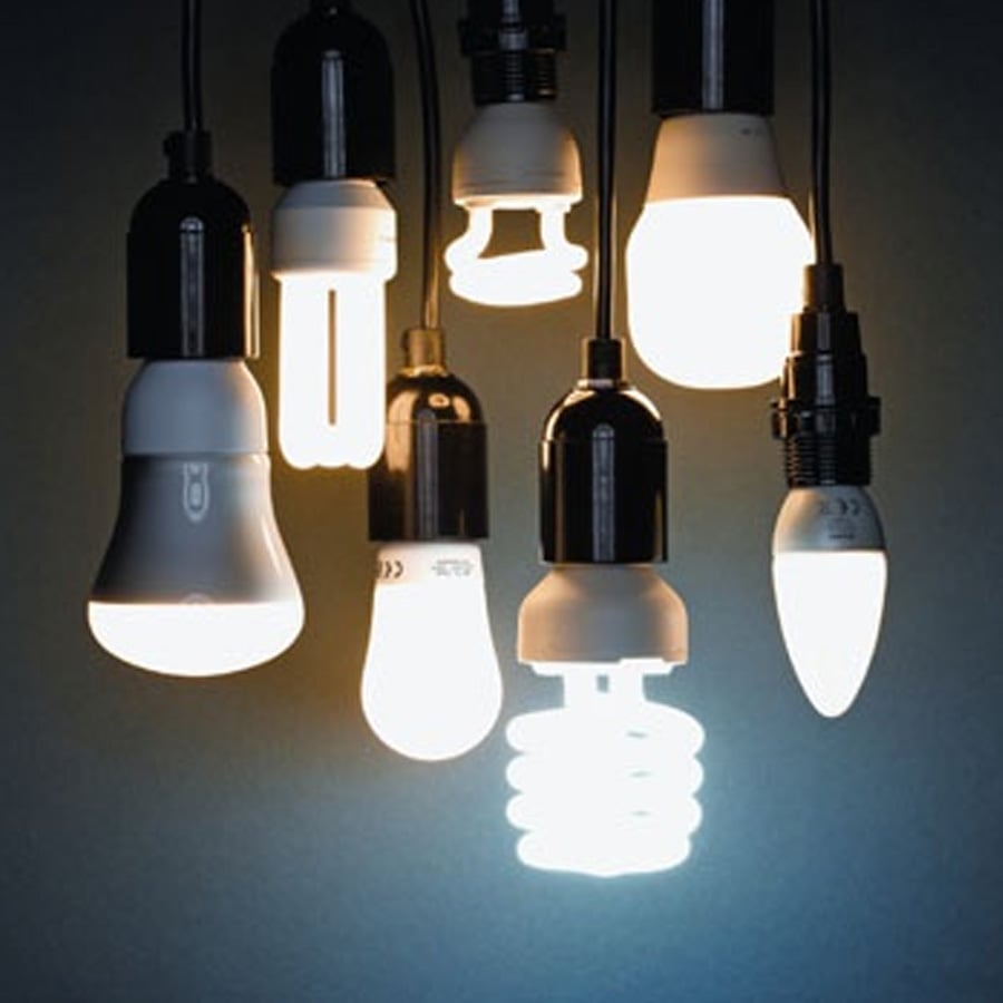 A group of various energy-efficient light bulbs, including LED and CFL types, are hanging lit against a dark background.