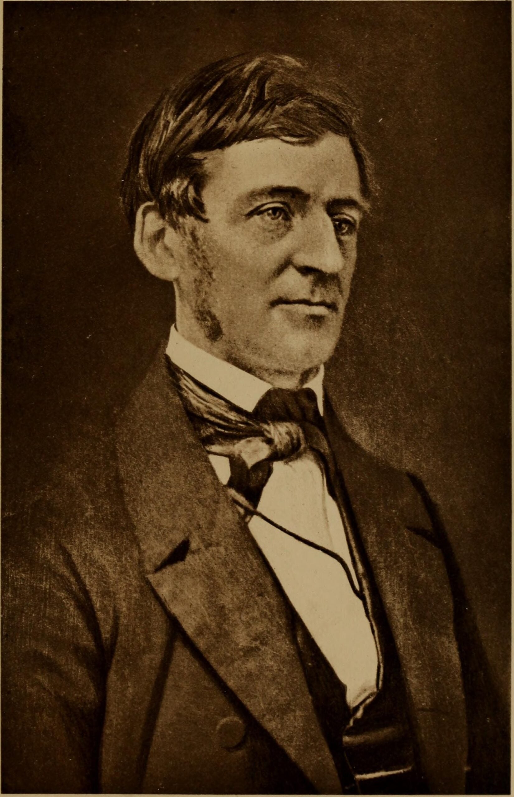 Sepia-toned portrait of a man with side-parted hair, wearing a suit, waistcoat, and bow tie, looking slightly to the side against a plain background.