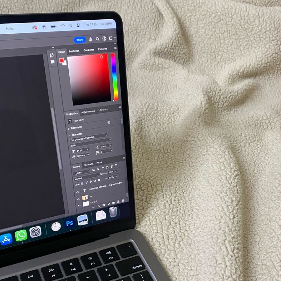 A laptop displaying a graphic editing program is positioned on a textured beige blanket. The screen shows color settings, while app icons are visible on the bottom dock.