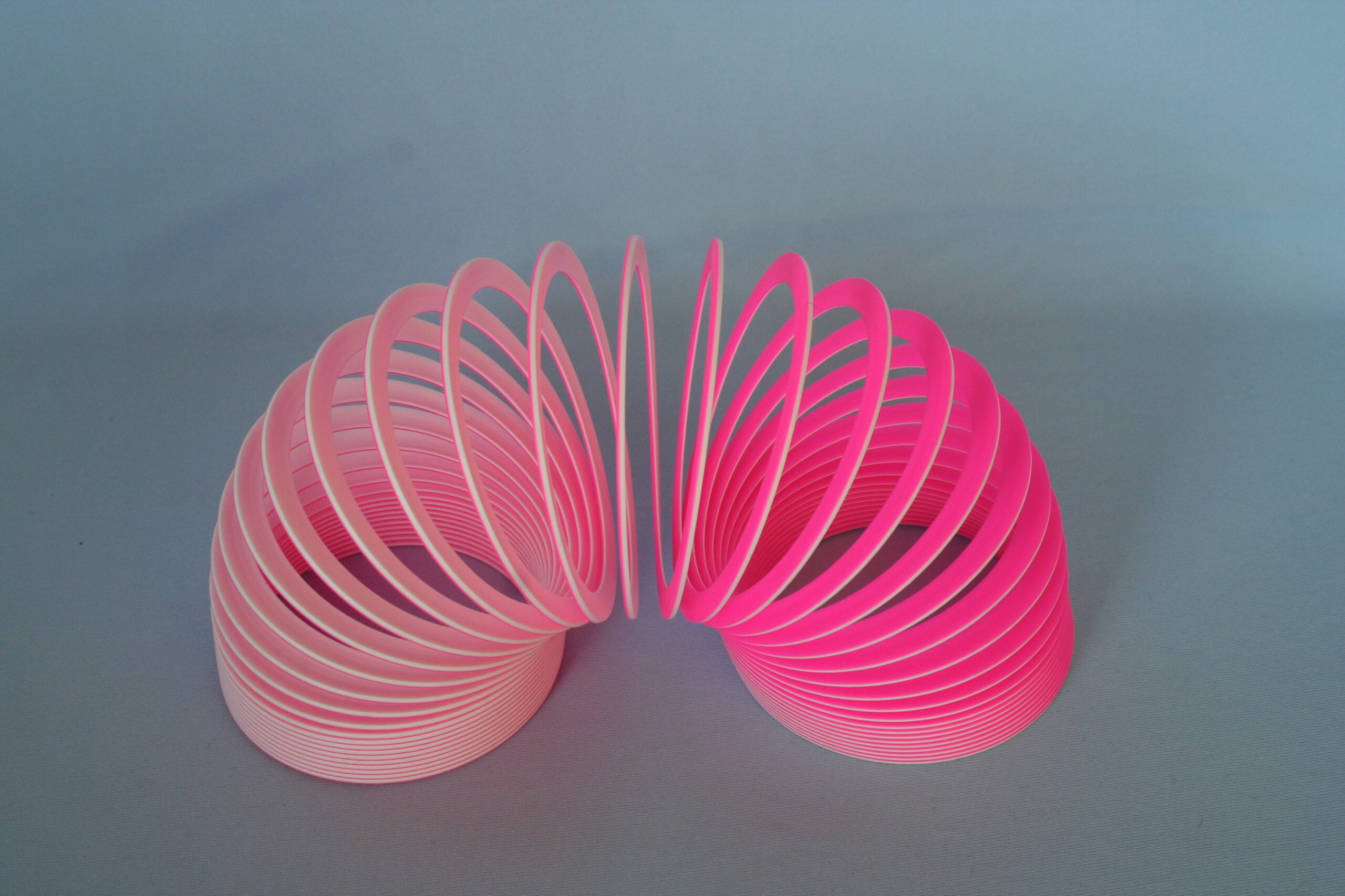 A pink plastic Slinky toy is spread out in an arch shape against a plain light blue background.