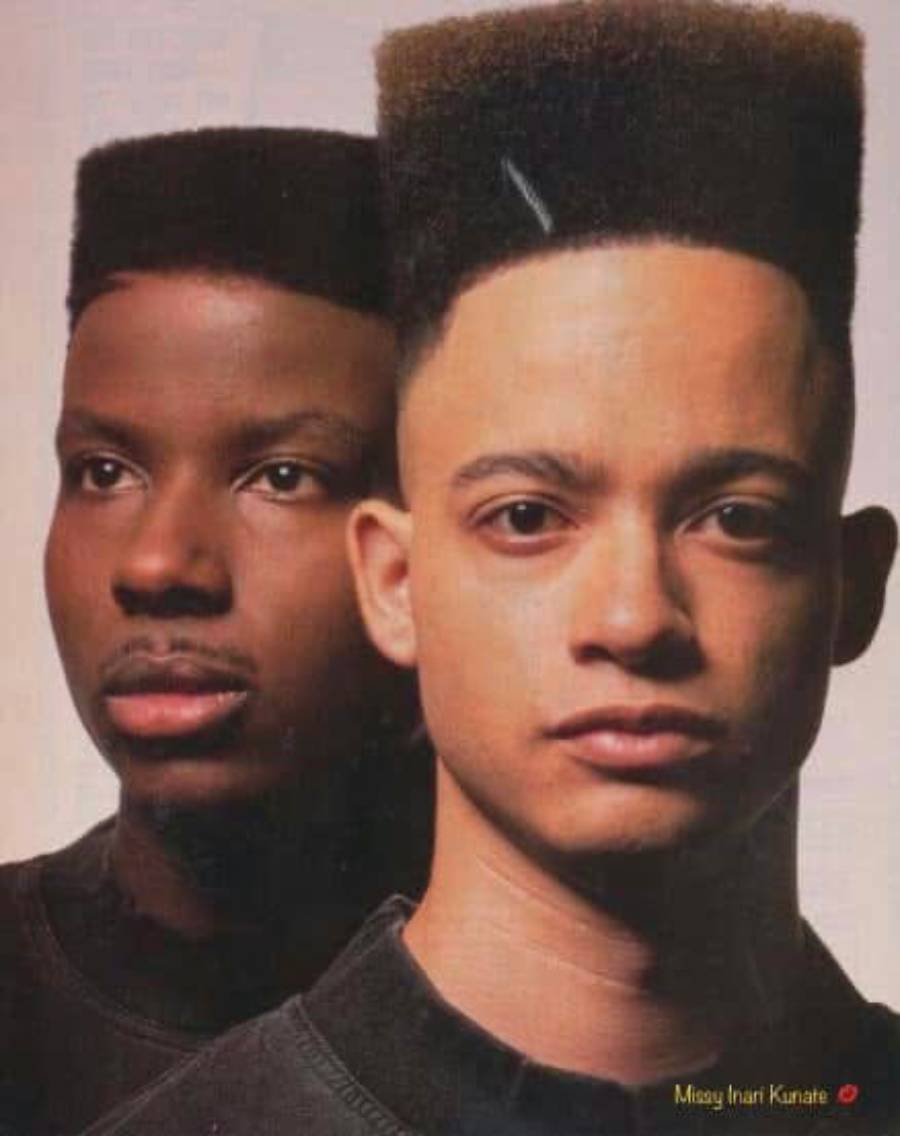 Two young men stand closely side by side, both with high-top fade haircuts, looking directly at the camera against a plain background.