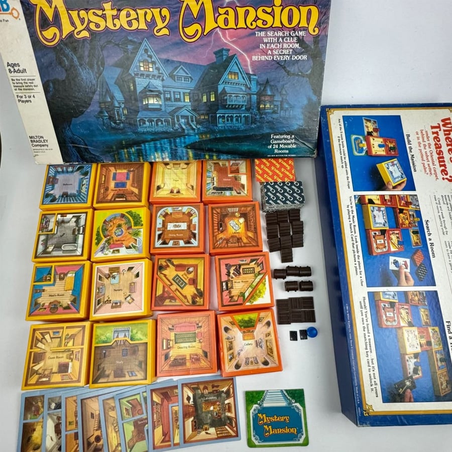 Mystery Mansion board game components, including room tiles, cards, tokens, dice, and the game box featuring artwork of a spooky mansion. The opened box lid is visible, showing setup instructions inside.