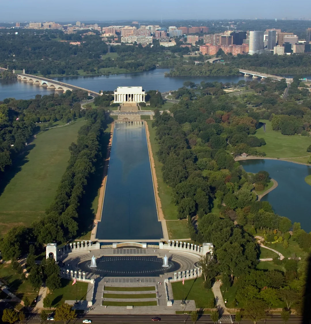 Aerial view of the National Mall in Washington, D.C., featuring the Lincoln Memorial, Reflecting Pool, World War II Memorial, and surrounding greenery with cityscape in the background.