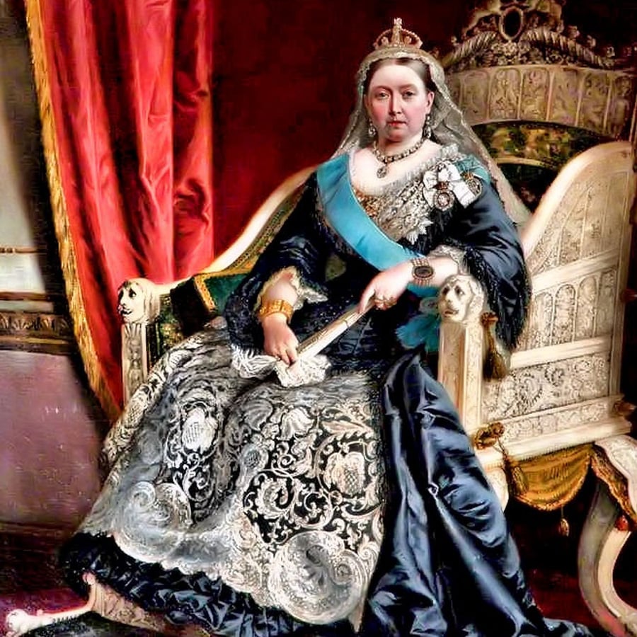 A regal woman in a crown and ornate dress sits on an elaborate throne, holding a fan. She wears a blue sash, medals, and jewelry, with rich red curtains and detailed furnishings in the background.