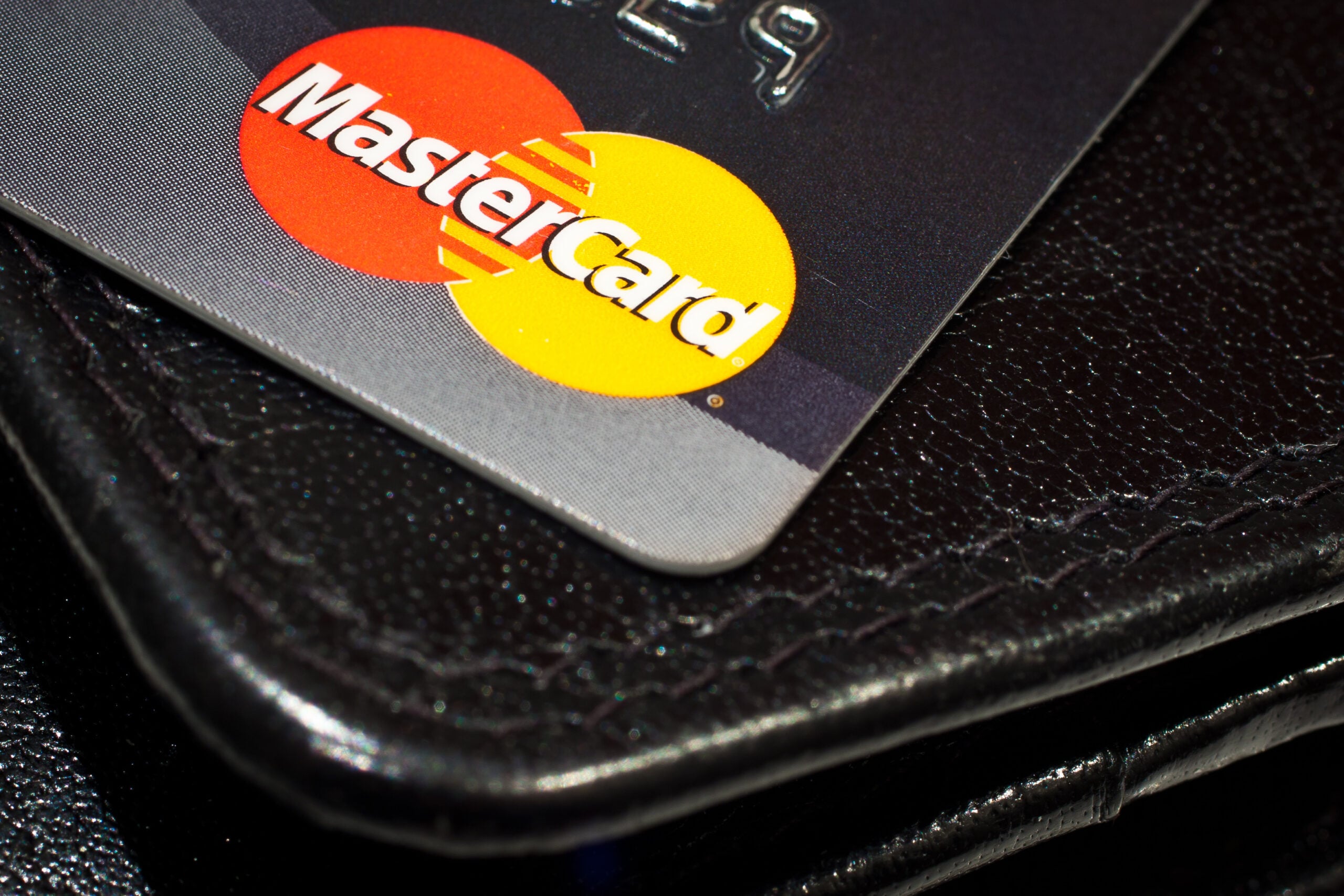 Close-up of a Mastercard credit card partially resting on a black leather wallet, showing the Mastercard logo clearly.