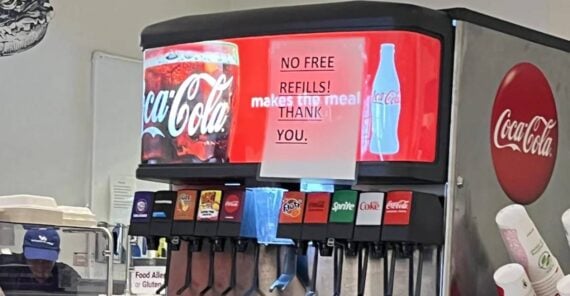 A Coca-Cola soda fountain with a bright red sign reading "NO FREE REFILLS! makes this meal THANK YOU," and various soda options, plastic cups, and an ice dispenser visible.