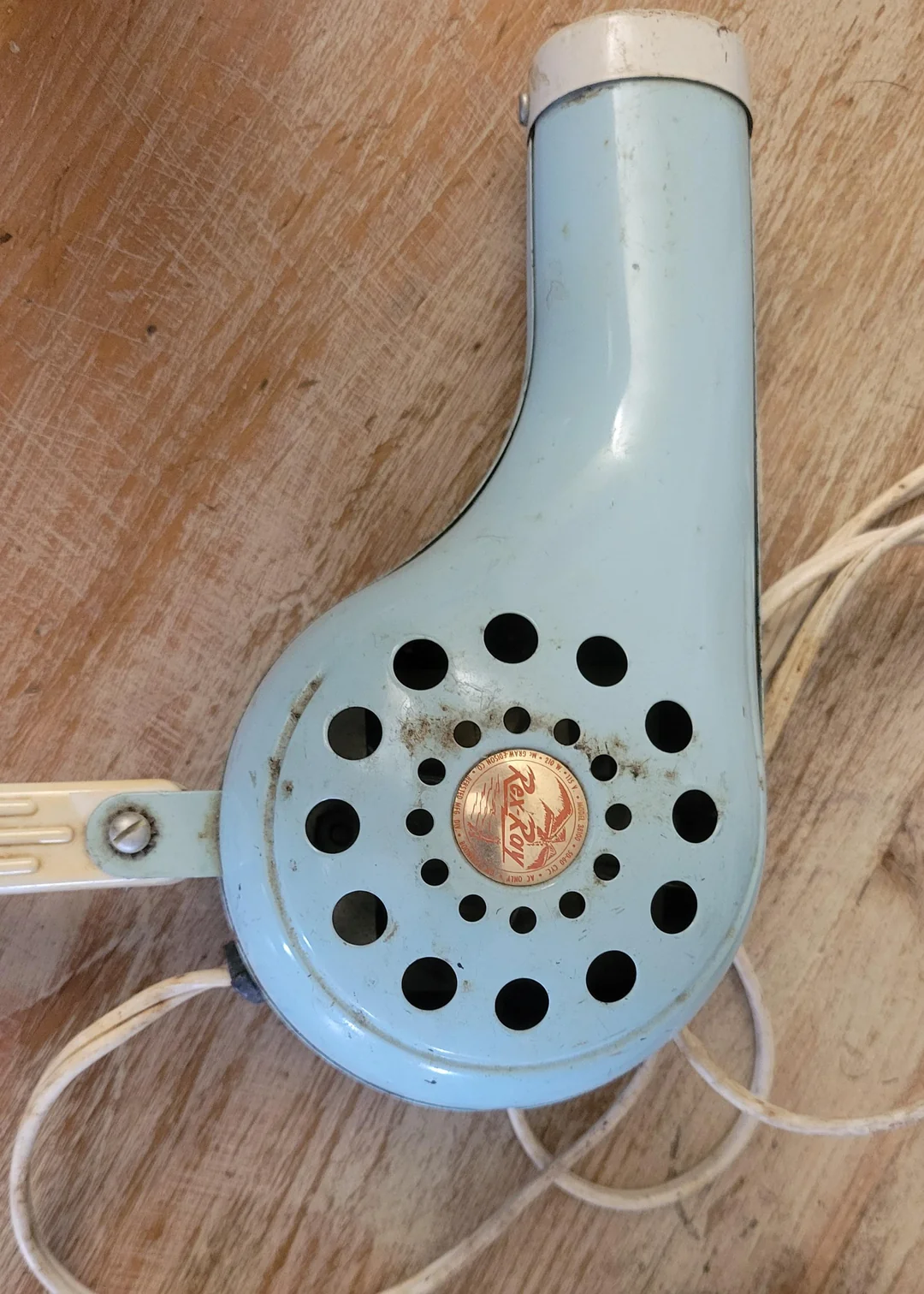 A vintage blue handheld hair dryer with circular vents, a white handle, and an electric cord, resting on a wooden surface.