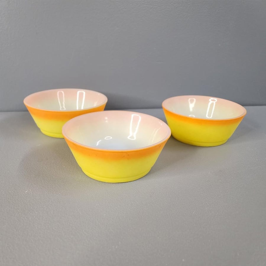 Three small ceramic bowls with a yellow base and light pink rims sit on a gray surface against a gray background.
