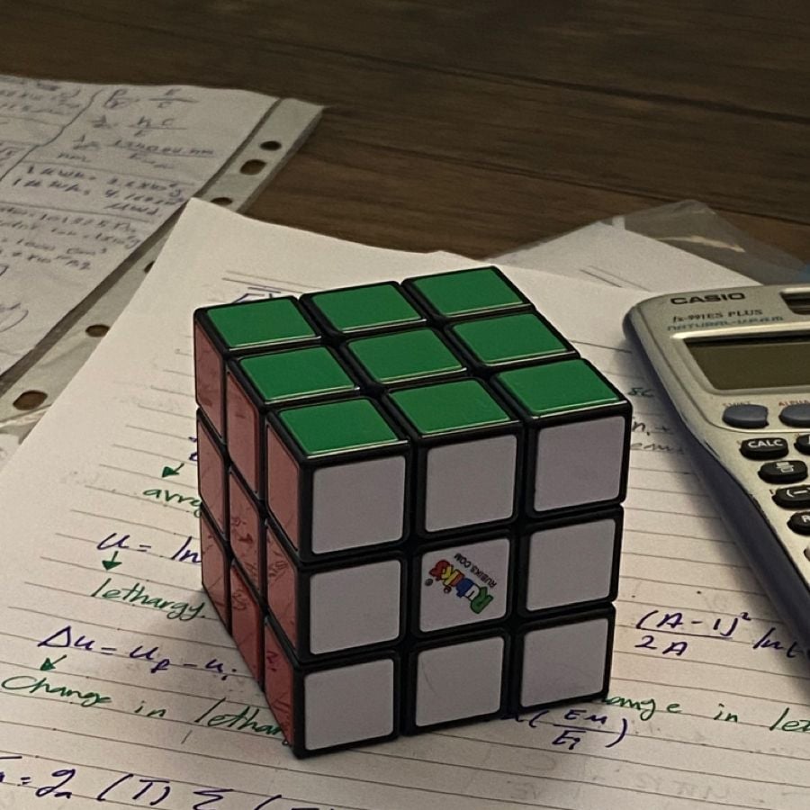 A solved Rubik’s cube sits on handwritten notes beside a scientific calculator and loose paper on a wooden table.