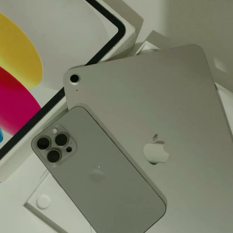 A silver iPhone and iPad are placed on top of their boxes, with part of the iPad screen visible showing colorful shapes.