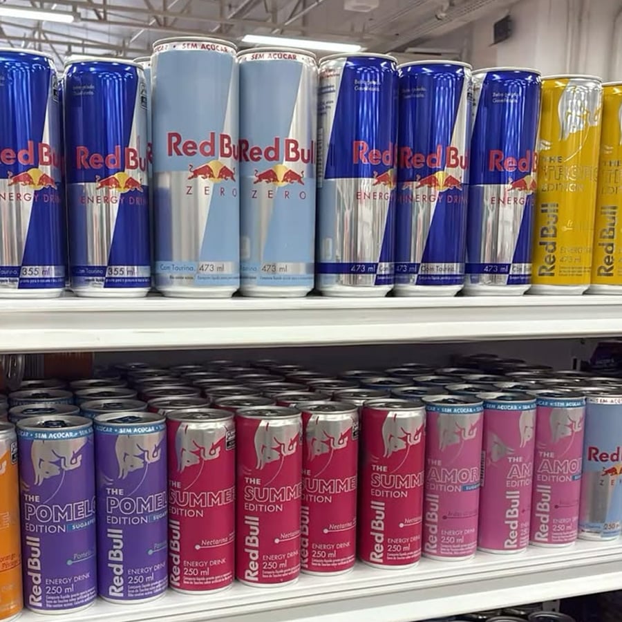 Shelves stocked with various Red Bull energy drink cans in different flavors and colors, including original, sugarfree, and special editions, all neatly organized in rows.