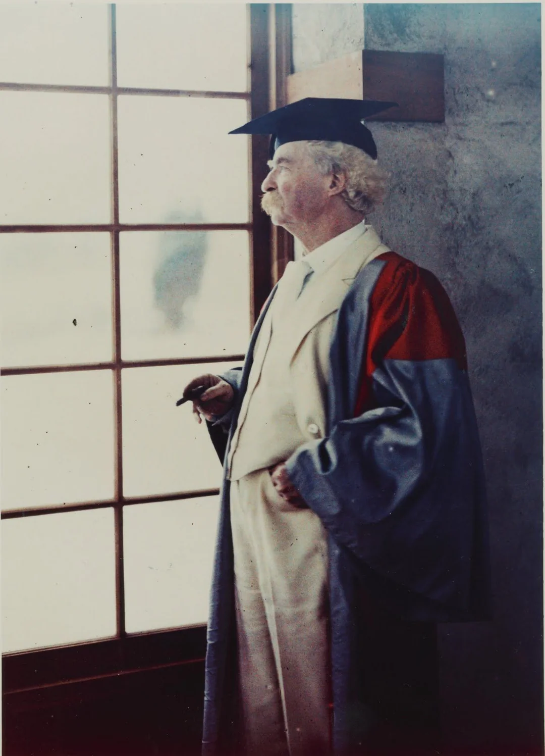 An older man with white hair and a mustache, wearing academic regalia and holding a cigar, stands by a window, looking outside.