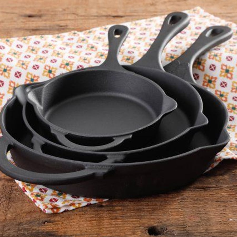 Three black cast iron skillets of different sizes are nested together on a patterned fabric, placed on a wooden surface.