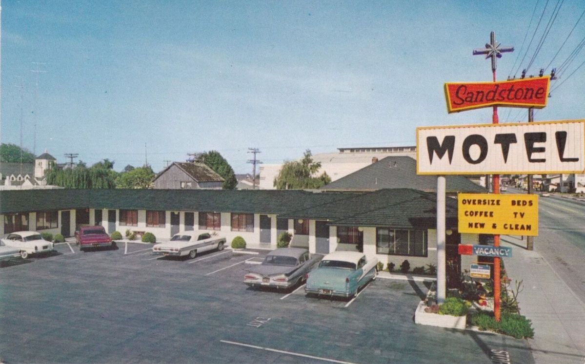 A vintage postcard shows the Sandstone Motel with classic cars parked in front. The motel sign advertises oversize beds, coffee, TV, and vacancy. The single-story building has a green roof and white exterior.