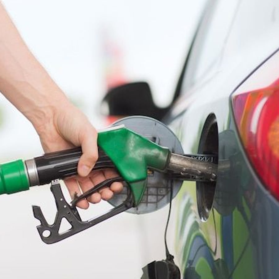 A person is refueling a car at a gas station, holding a green fuel nozzle inserted into the vehicle’s gas tank.