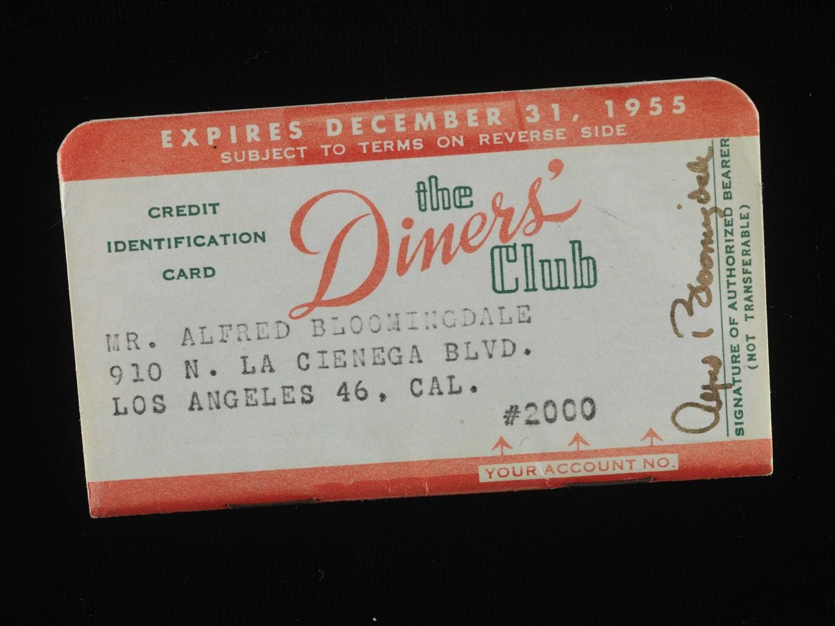 Vintage Diners’ Club credit card with red text, expiration date of December 31, 1955, and the name Mr. Alfred Bloomingdale, 910 N. La Cienega Blvd., Los Angeles, CA. Signature and account number 2000 visible.
