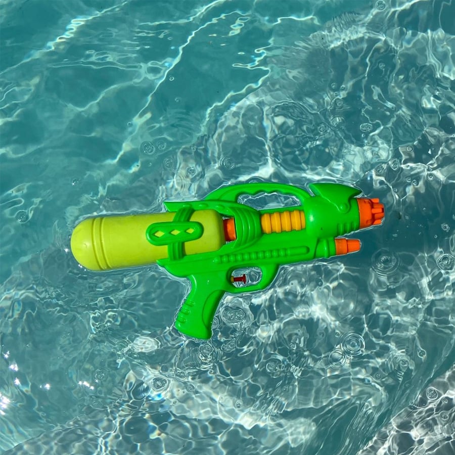 A green and orange plastic water gun floating on the surface of a clear blue pool.