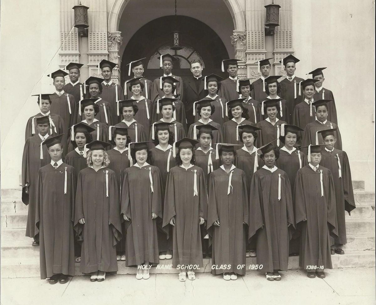 Black and white photo of a large group of students in graduation gowns and caps, posing on steps outside a building. A few adults stand behind them. Text at the bottom reads "Holy Name School Class of 1950.