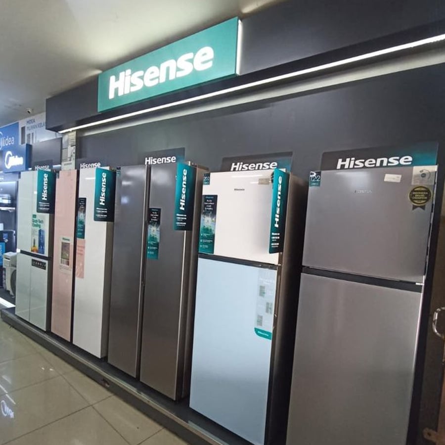 A row of Hisense refrigerators in various sizes and colors is displayed in a brightly lit appliance store, with a large illuminated Hisense sign above them.