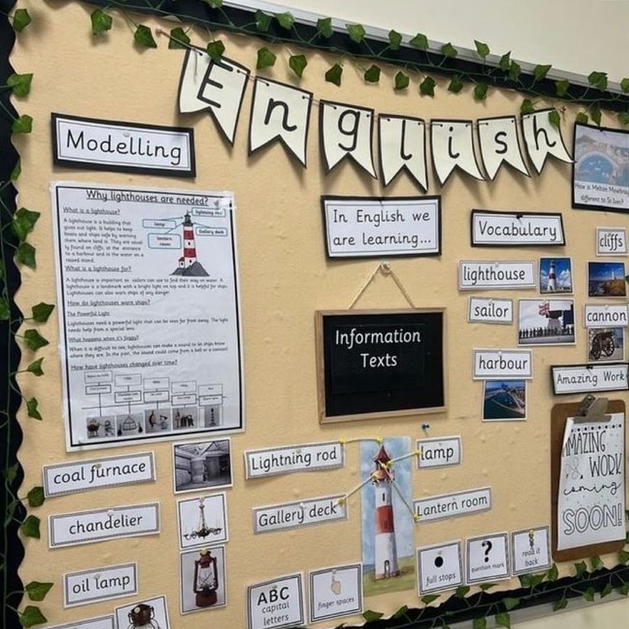 A classroom bulletin board displays English topics on information texts, focusing on lighthouses, with vocabulary cards, images, and printed explanations. Decorative banners and green faux vines frame the display.