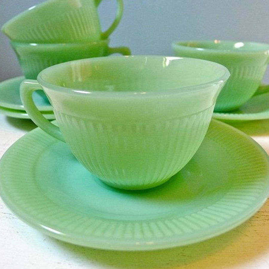 Four pale green vintage glass teacups with matching saucers are arranged on a white surface, with the focus on the cup and saucer at the front.