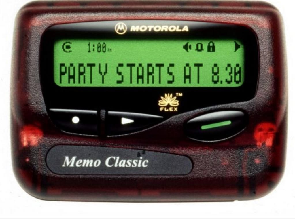 A Motorola Memo Classic pager displays a message on its green screen: “PARTY STARTS AT 8.30.”