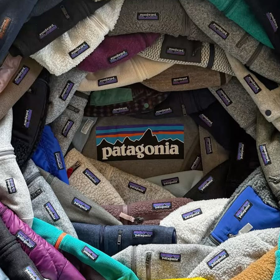 Various Patagonia jackets arranged in a spiral, showcasing many visible Patagonia tags, with a large Patagonia logo in the center. Sweater textures and colors vary from gray, blue, green, brown, and purple.