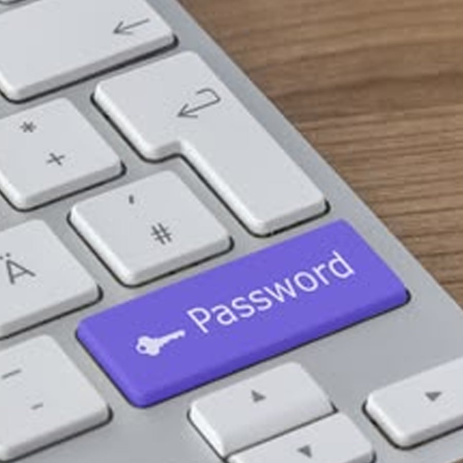 A computer keyboard with a purple key labeled "Password" and a key icon, replacing the usual return key. The keyboard is on a wooden surface.
