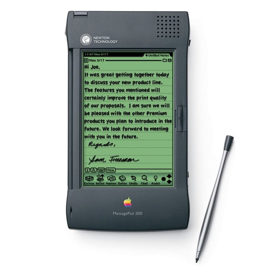 A vintage Apple MessagePad 2000 with a stylus displays a handwritten note on its green screen. The device features a black case and multiple physical buttons below the screen.