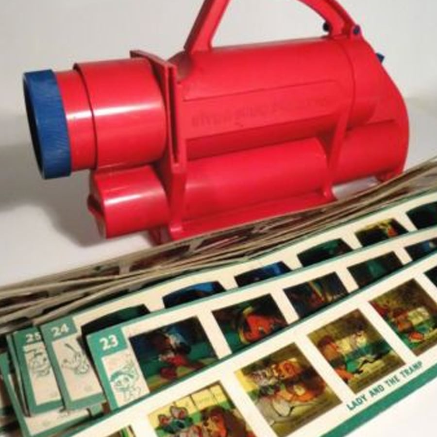 A red vintage viewfinder toy sits behind several rows of film reels featuring colored cartoon images and numbers, including scenes from “Lady and the Tramp.”