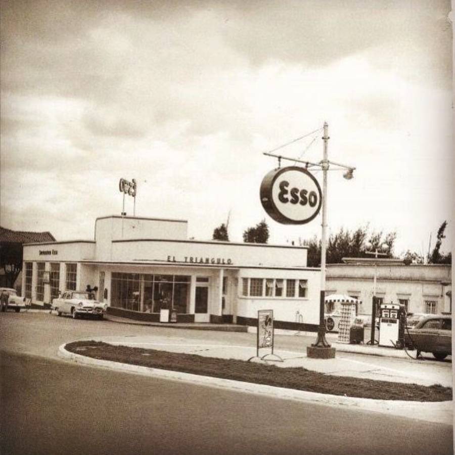 A vintage black-and-white photo of an Esso gas station named "El Triángulo," with old cars parked nearby and classic gas pumps visible under a cloudy sky.