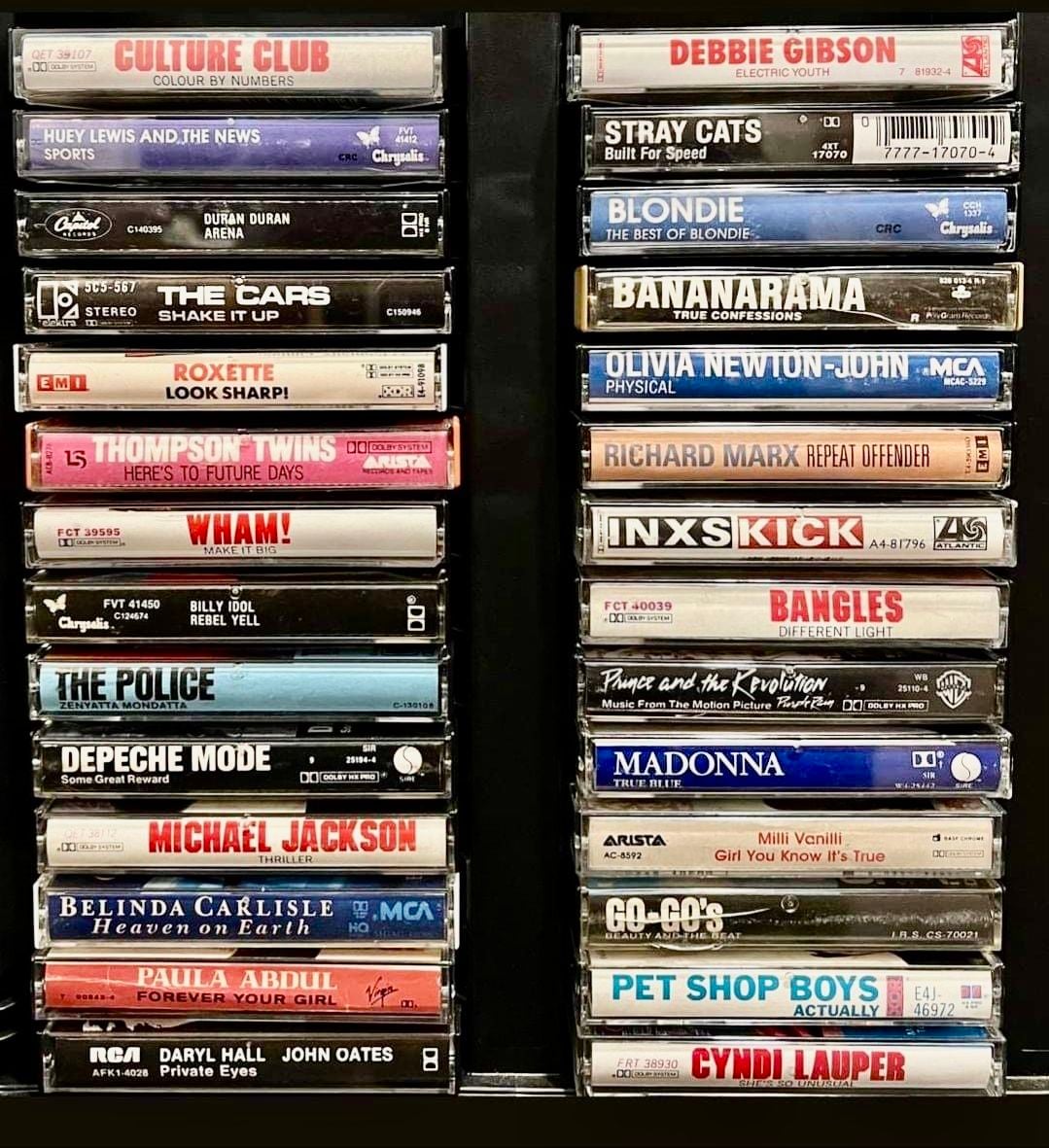 Two columns of vintage cassette tapes in cases, featuring artists like Culture Club, Duran Duran, INXS, Madonna, Michael Jackson, Cyndi Lauper, Wham!, Blondie, The Police, and Debbie Gibson.