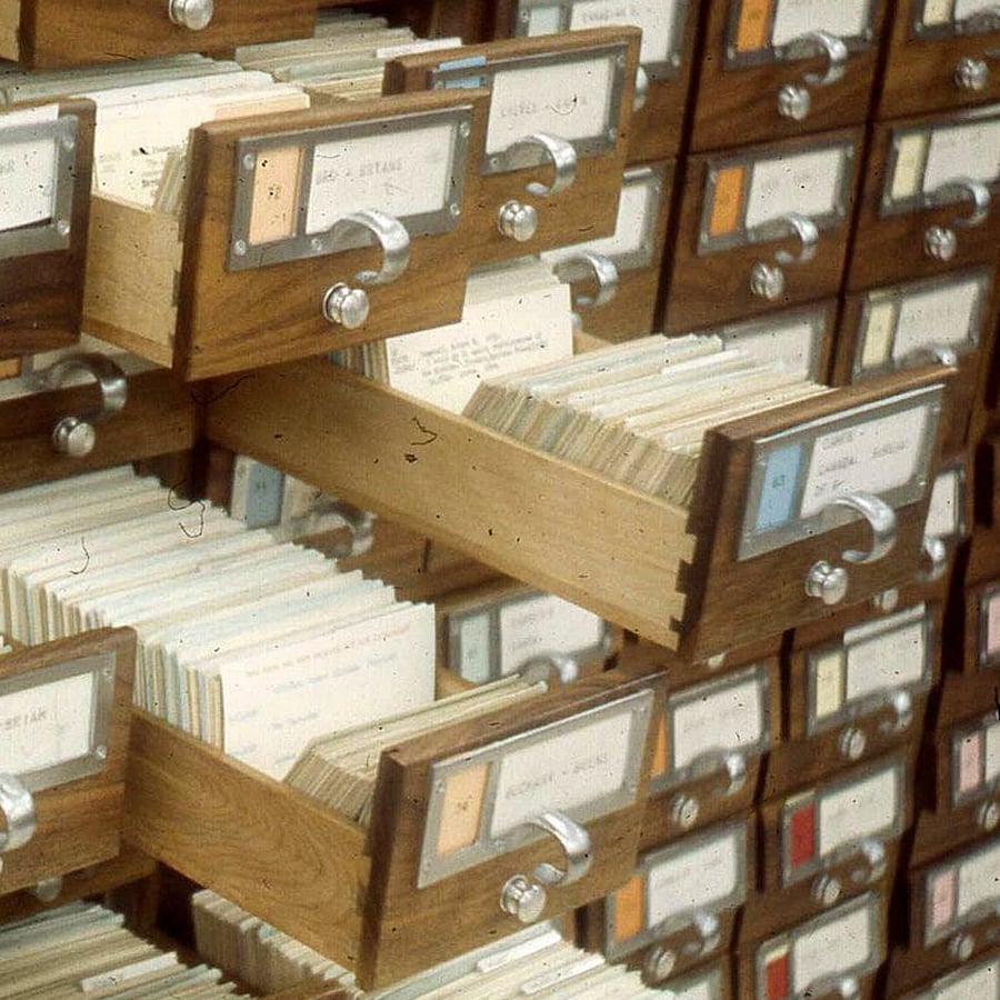 Wooden library card catalog drawers are open, revealing rows of index cards with typed labels.