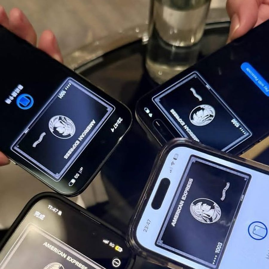 Four smartphones display digital American Express cards as people hold them together over a reflective table, suggesting a social gathering or group payment scenario.