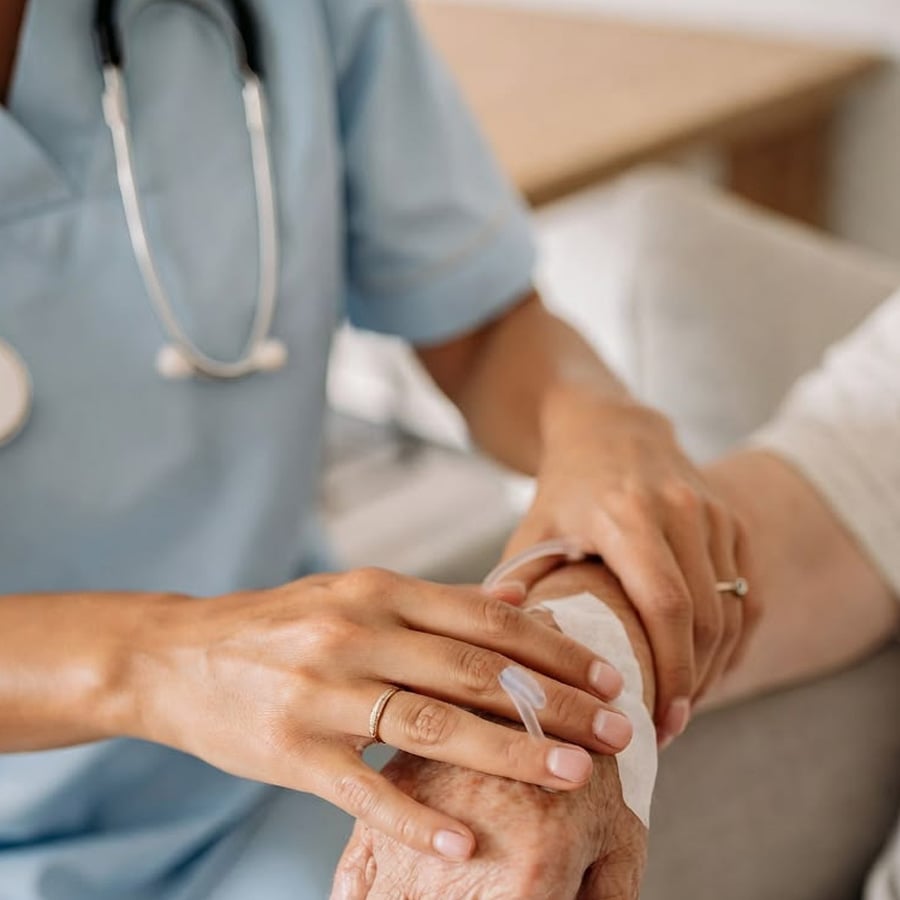 A healthcare worker in scrubs gently places a bandage on an elderly person's hand, providing care and support.
