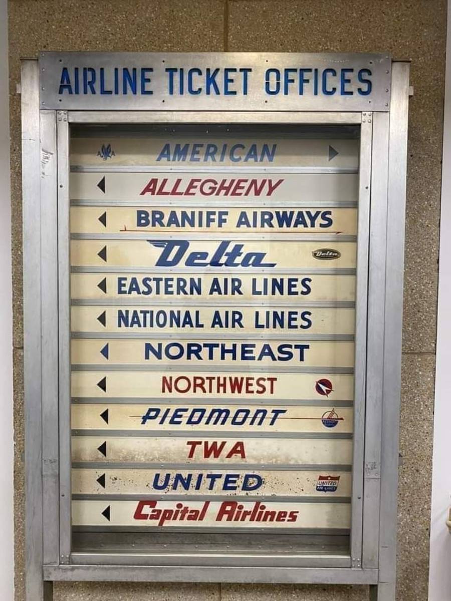 A vintage sign lists various airline ticket offices, including American, Allegheny, Braniff Airways, Delta, Eastern Air Lines, National Air Lines, Northeast, Northwest, Piedmont, TWA, United, and Capital Airlines.