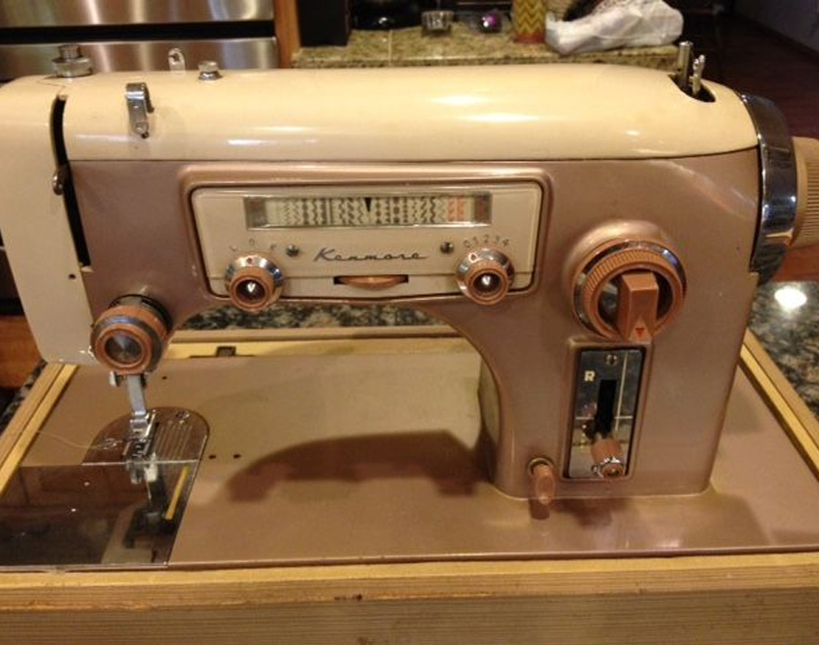 A vintage Kenmore sewing machine in beige and brown sits on a wooden table, featuring dials, levers, and a needle area visible at the front.