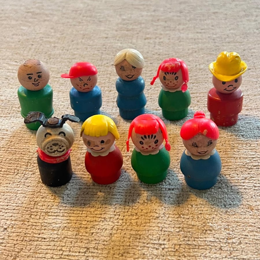 Nine vintage Fisher-Price Little People figurines, including children, a dog, and a firefighter, are arranged on a beige textured surface.