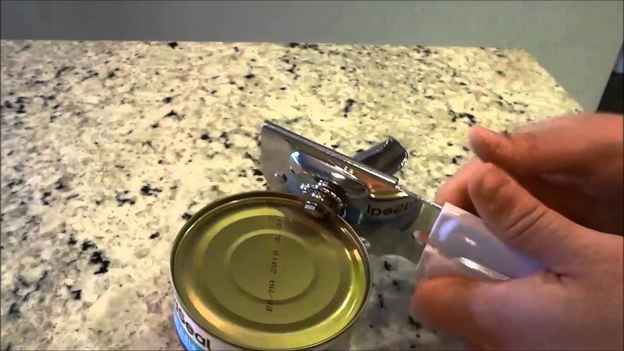 A hand uses a manual can opener to open a metal can on a speckled granite countertop.