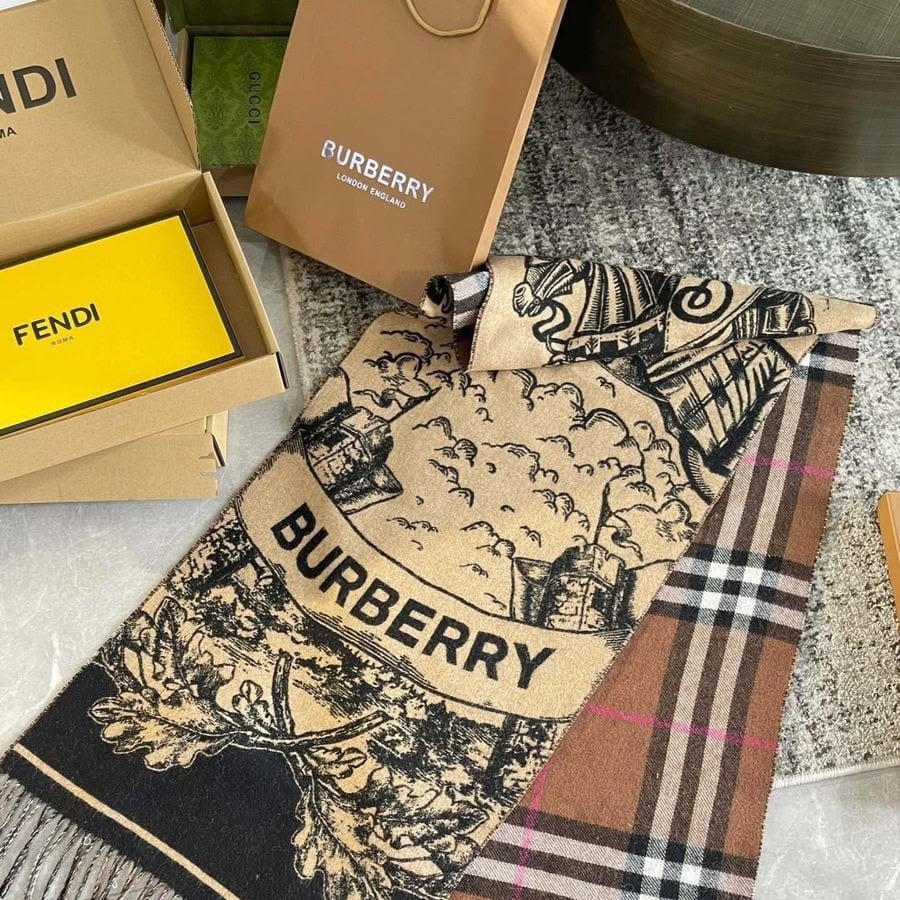 A Burberry scarf with a check pattern and artistic black design is displayed next to Burberry and Fendi packaging on a table.