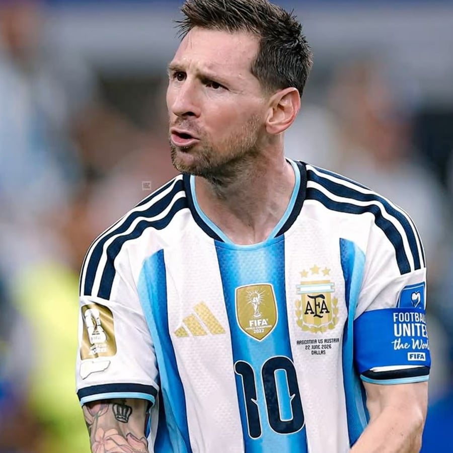 A male soccer player in Argentina's national team jersey with the number 10 and a blue captain's armband is on the field, looking focused and expressive.