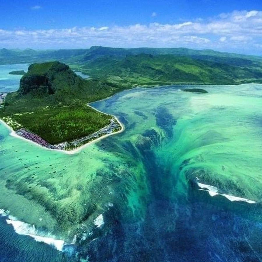 Aerial view of Le Morne Brabant in Mauritius with an underwater illusion that appears as a waterfall, created by sand and silt deposits in the turquoise ocean near the coast.