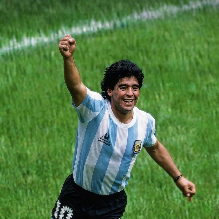 A soccer player in an Argentina jersey celebrates on a grassy field, smiling with one arm raised in victory.